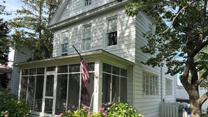 A two-story house with a covered porch, a number '108' on the side, and a small garden with pink flowers. - 3-bedroom historic vacation home newly renovated in the middle of Oxford MD. (Oxford)