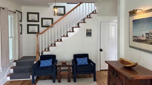 A staircase with wooden steps and a white railing, leading to a door. There are two armchairs with blue cushions and a small wooden table with a bowl. - 3-bedroom historic vacation home newly renovated in the middle of Oxford MD. (Oxford)