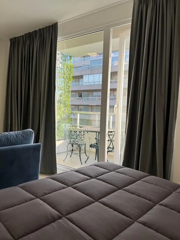Ein Schlafzimmer mit einem großen Bett, dunklen Vorhängen und einem Blick auf einen Außenbalkon mit Tisch und Stühlen.