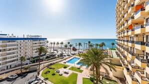 A high-rise hotel with a pool area, palm trees, and a view of the sea. - MalagaSuite New Aloha Playa (Benalmádena)