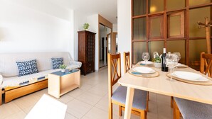A modern living room with a sofa, a wooden cabinet, and a dining table set for four. - MalagaSuite New Aloha Playa (Benalmádena)