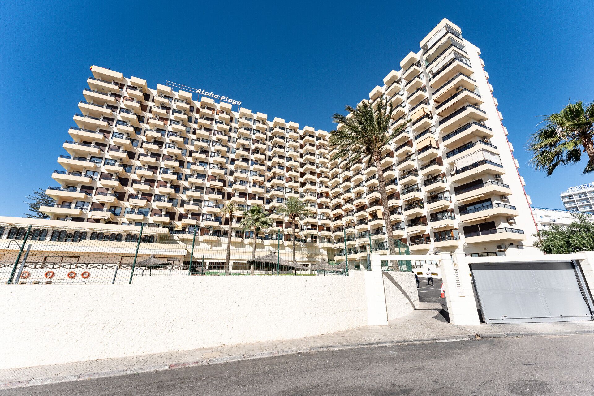 Un hôtel de grande hauteur doté de nombreux balcons, un ciel dégagé et un palmier au premier plan.