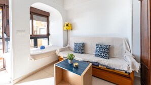 A cozy living room with a sofa, two patterned cushions, a small coffee table with a plant, and a window with a view. - MalagaSuite New Aloha Playa (Benalmádena)