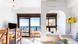 A modern living room with a TV, wooden chairs, a sofa, and a balcony with a view of the sea. - MalagaSuite New Aloha Playa (Benalmádena)