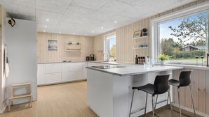 A modern kitchen with a central island, bar stools, wooden paneling, and a view of the outdoors.