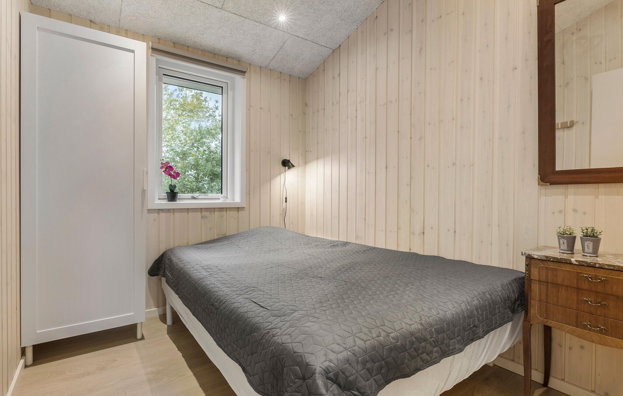 Et soveværelse med seng, et vindue med udsigt, en senget lampe og en trækommode.