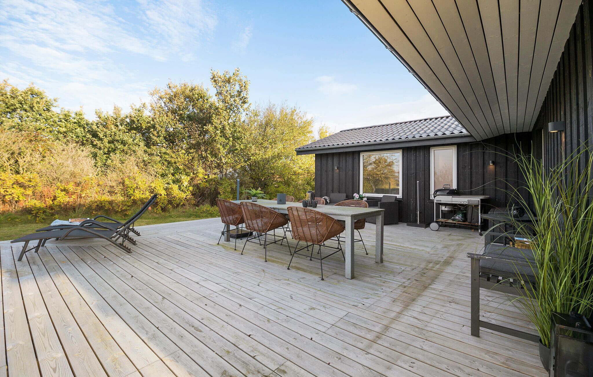 A wooden deck with outdoor furniture, a grill, and a large window overlooking a forested area.