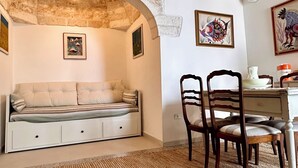 Um quarto aconchegante com parede de pedra, um banco estofado, uma mesa de jantar com cadeiras e um lustre.