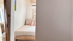 Quarto com cama, teto com vigas de madeira e porta que dá para outro cômodo.