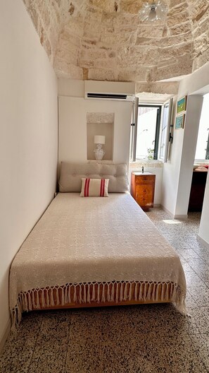 Een slaapkamer met een bed, een nachtkastje, een lamp en een raam.