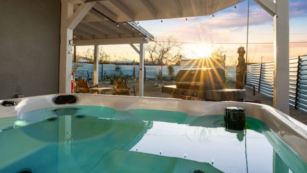A hot tub with a view of the sunset and a barbecue grill.