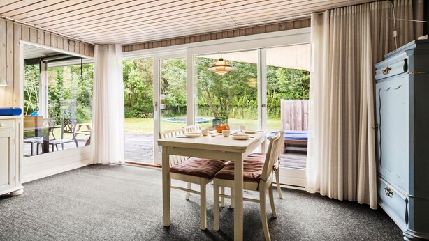 A room with a dining table and chairs, a kitchen area with a refrigerator, and large windows offering a view of the outdoors. - Lovely home in Nykøbing Sj with WiFi (Nykøbing Sj)