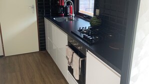 A compact kitchen with a black countertop, white cabinets, a built-in oven, and a window providing natural light. - Charming dog-friendly lodge in, Veluwe. Enjoy the nature by walking or cycling. (Putten)