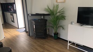 A modern living room with a white sofa, a black TV stand, a wooden floor, a black stove, and a potted plant. - Charming dog-friendly lodge in, Veluwe. Enjoy the nature by walking or cycling. (Putten)