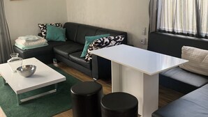 A modern living room with a white coffee table, black ottomans, a black sofa with patterned cushions, and a white ceiling fan. - Charming dog-friendly lodge in, Veluwe. Enjoy the nature by walking or cycling. (Putten)