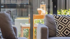A modern living room with two grey sofas, a wooden coffee table, and a large window offering a view of a balcony with a table and plants. - Explore Wanaka - A Stylish Unit That Guests Adore! (Albert Town)