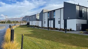 A row of modern, two-story buildings with a flat roof design, arranged in a linear fashion along a paved pathway. - Explore Wanaka - A Stylish Unit That Guests Adore! (Albert Town)