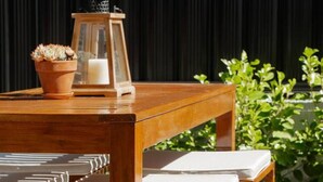 A wooden outdoor dining set with cushioned chairs and a table, accompanied by a lantern and a potted plant. - Explore Wanaka - A Stylish Unit That Guests Adore! (Albert Town)