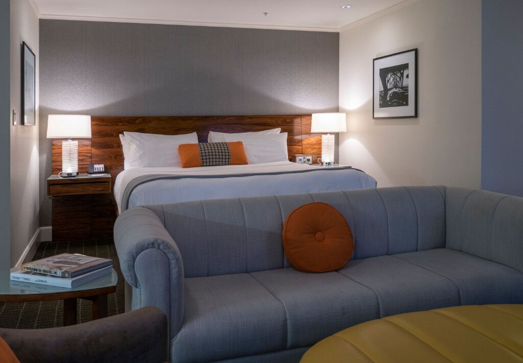 A hotel room with a bed, two bedside tables, a sofa, and a small table with a lamp.