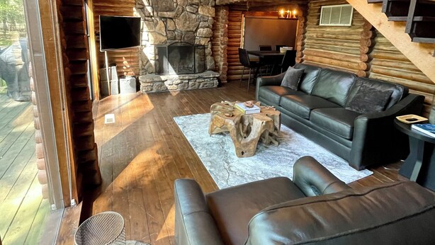 Ein gemütliches Blockhaus-Interieur mit Kamin aus Stein, Ledersofas und einem Kronleuchter.