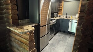 Eine Küchenzeile in einer Blockhütte mit einem Edelstahl-Kühlschrank, einer Mikrowelle und einem Backofen.
