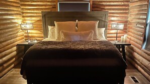 Ein Schlafzimmer in einer Blockhütte mit einem großen Bett, zwei Nachttischen mit Lampen und einem Fenster.