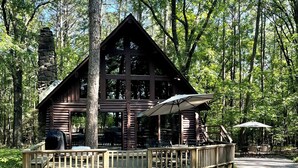 Eine rustikale Holzhütte mit einem Steinofen, großen Fenstern und einer Holzterrasse mit Sitzgelegenheit im Freien.