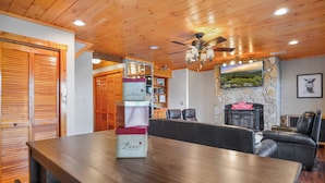 Una habitación con paneles de madera, una mesa de comedor, sillas de cuero, una chimenea y un televisor montado.