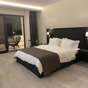 A hotel room with a large bed, a chair, a nightstand, and a view through a glass door. - The Reference Club Restaurant & Accommodation (Luleburgaz)