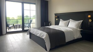 A modern hotel room with a large bed, a balcony with chairs, and a view of greenery. - The Reference Club Restaurant & Accommodation (Luleburgaz)