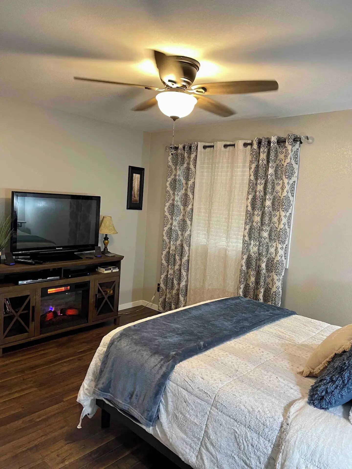 Une chambre à coucher avec un lit, un ventilateur de plafond, une télévision et une armoire en bois.