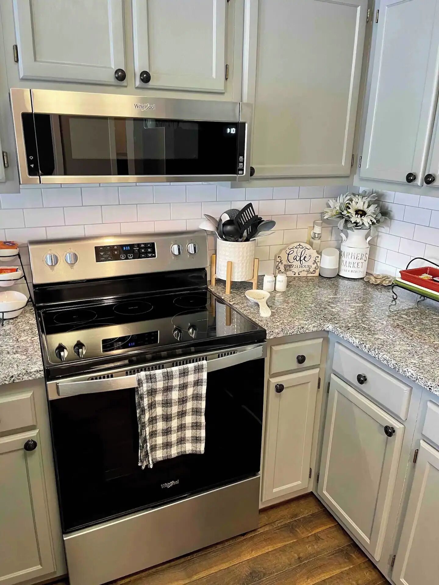 Una cocina con estufa de acero inoxidable, microondas, armarios blancos y encimera de granito.