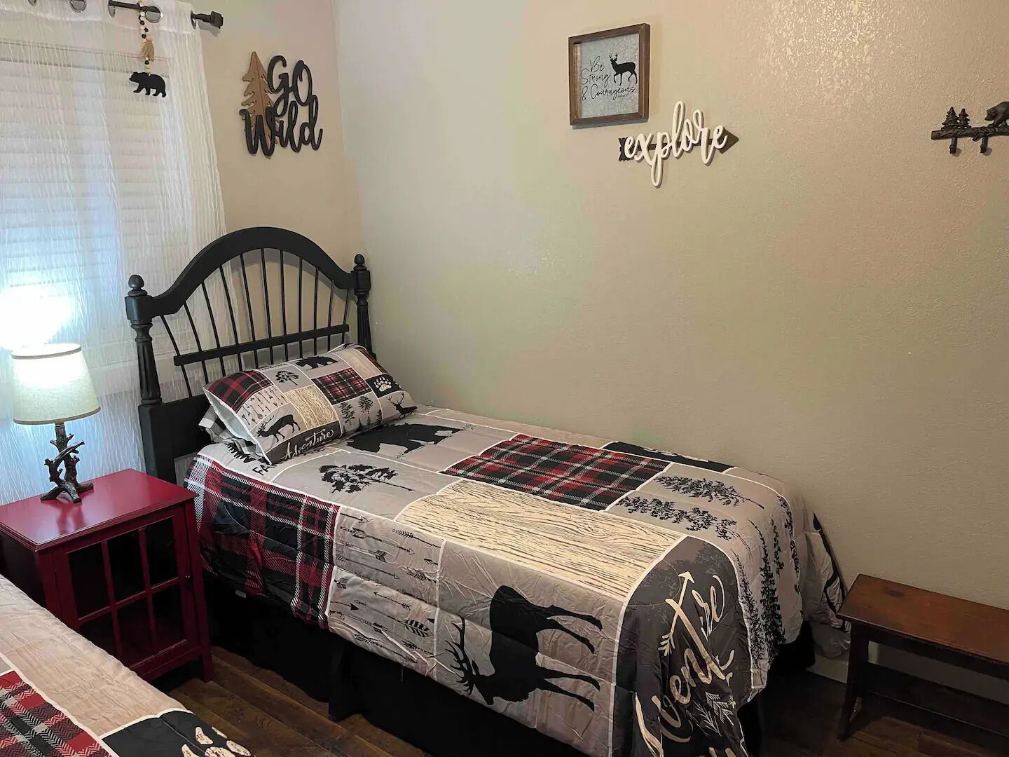 Un dormitorio con una cama, una mesita de noche, una lámpara, un banco y adornos en la pared, incluyendo un cuadro enmarcado y un letrero.