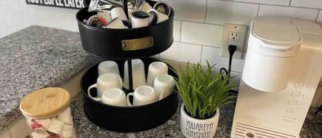 A kitchen counter with a coffee maker, a mug holder, a plant, and a jar of coffee pods.