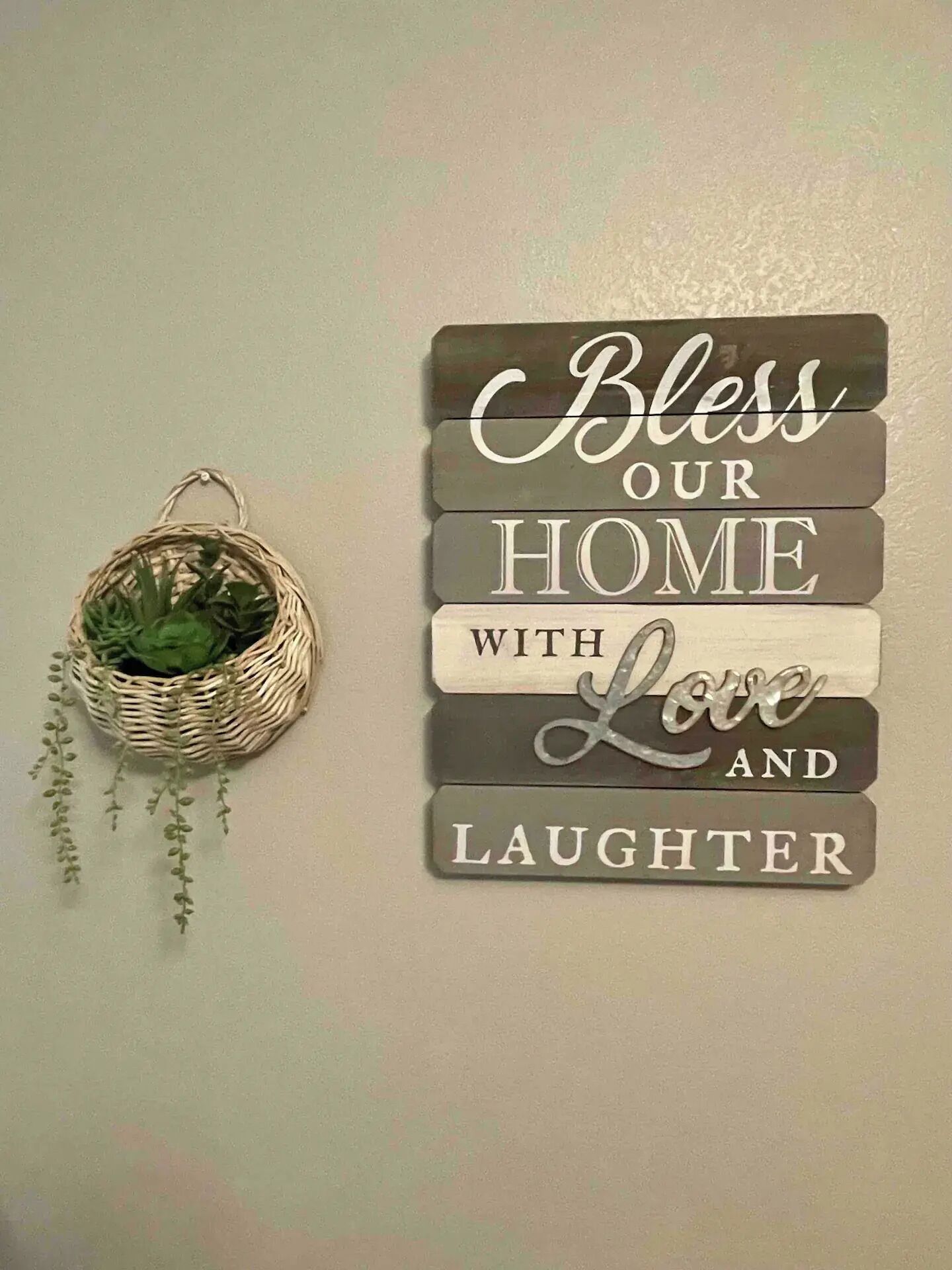 A wall decoration with the phrase "Bless our home with love and laughter" and a small wicker basket with hanging plants.
