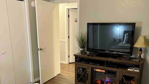 Un dormitorio con una cama, un televisor sobre un soporte de madera, una lámpara y una chimenea.