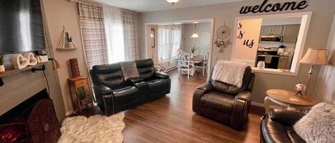 A living room with a sofa, a chair, a fireplace, and a 'welcome' sign.