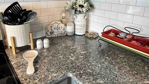 Una cocina con armarios blancos, encimera de granito, rincón para café y una bandeja roja con alimentos.