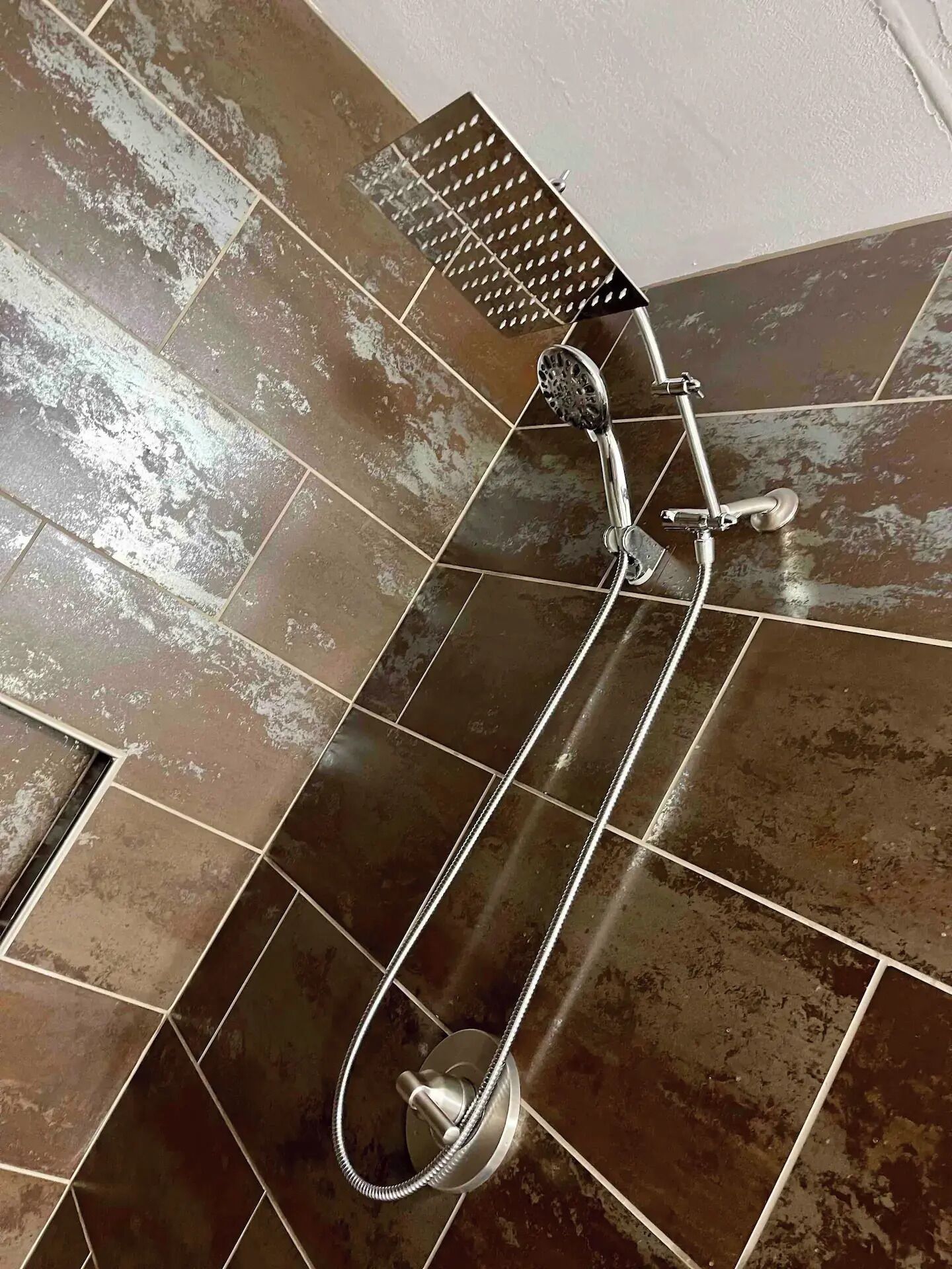 A shower with a handheld showerhead and a wall-mounted control valve.
