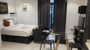 A modern hotel room with a bed, a desk, a chair, and a dining table. - Embassy garden ebs legend luxury studio  (Accra)