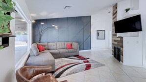 A modern living room with a sectional sofa, a leather armchair, a flat-screen TV mounted on the wall, and a fireplace.