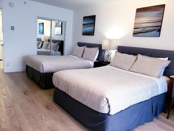 A hotel room with two beds, a mirror, a nightstand with a lamp, and artwork on the walls. - Beachfront Condo with Balcony&Kitchenette (Miami)