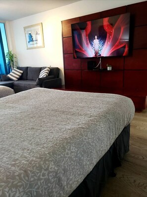 A hotel room with a large bed, a sofa, a TV mounted on a red wall, and a framed picture on the wall. - Beachfront Condo with Balcony&Kitchenette (Miami)