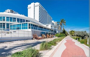 A modern hotel with a curved facade, large windows, and a red pathway leading to the entrance. - Beachfront Condo with Balcony&Kitchenette (Miami)