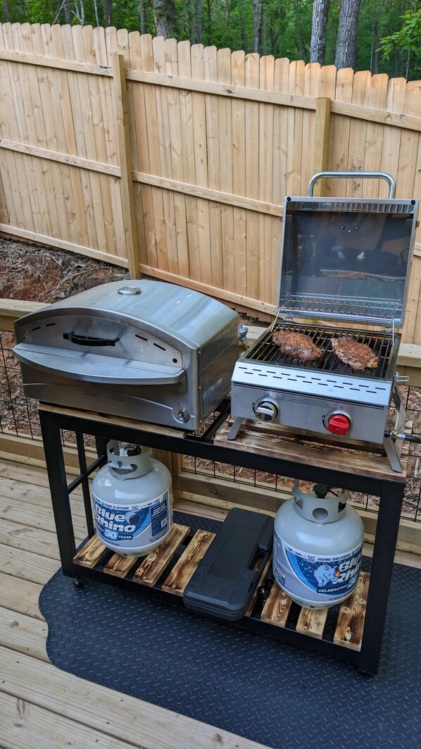A portable grill with two propane tanks, a griddle, and a smoker.