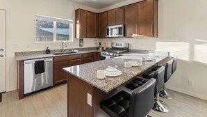 Una cocina moderna con encimeras de granito, electrodomésticos de acero inoxidable, armarios de madera y una isla central con taburetes de bar.