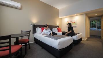 Une chambre d’hôtel avec un lit, un bureau et une chaise. Il y a un tableau au mur et une fenêtre donnant sur des arbres.