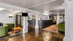 A lobby with a reception desk, green seating, a wooden bench, and a patterned carpet. -  Carnmore Hotel Lower Hutt (Lower Hutt)