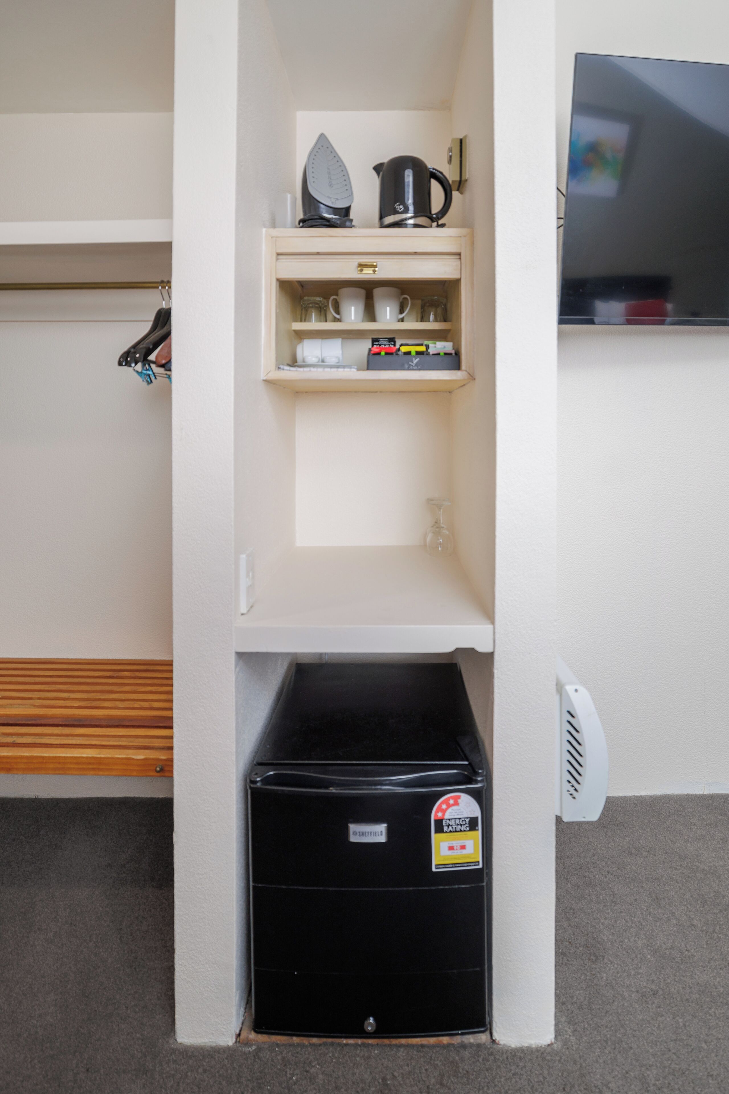 A kitchenette with a coffee maker, kettle, and shelves containing cups and a glass.