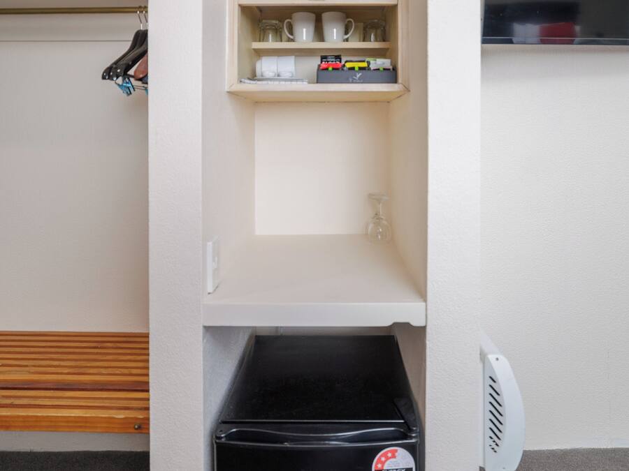 A kitchenette with a coffee maker, kettle, and shelves containing cups and a glass.